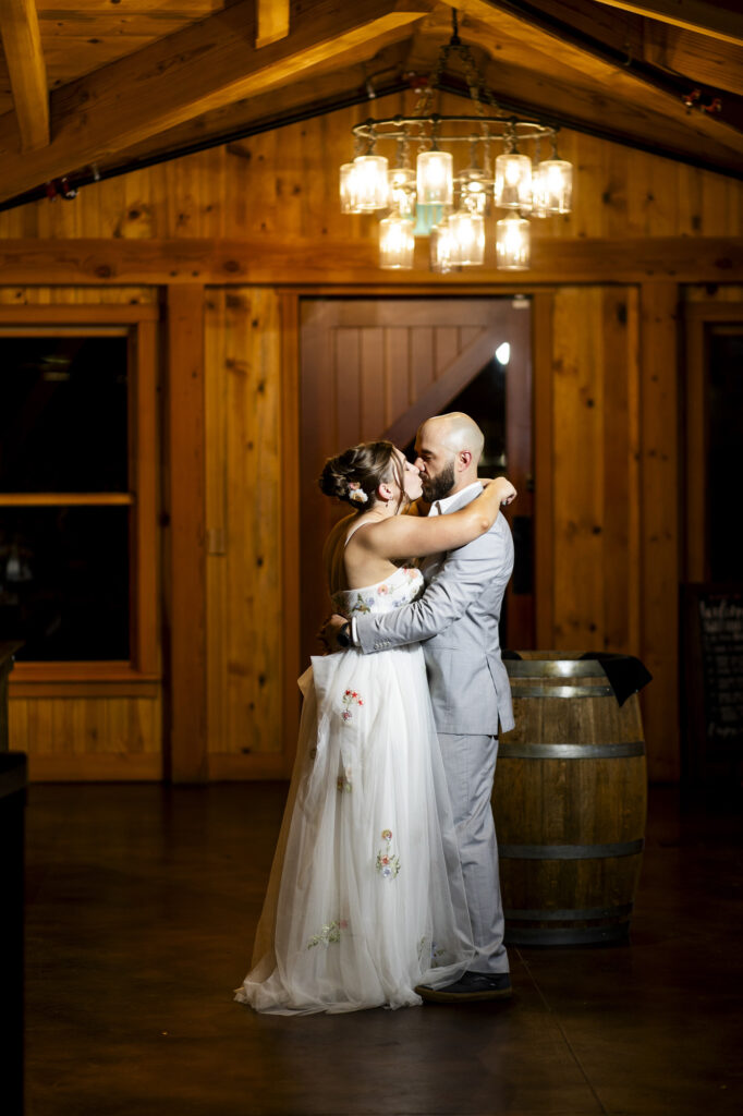 Bride and groom embrace and share a kiss in a warm wood paneled rustic venue with a chandelier overhead for wedding coverage Colorado Wedding Photographer Colorado Wedding Photographer