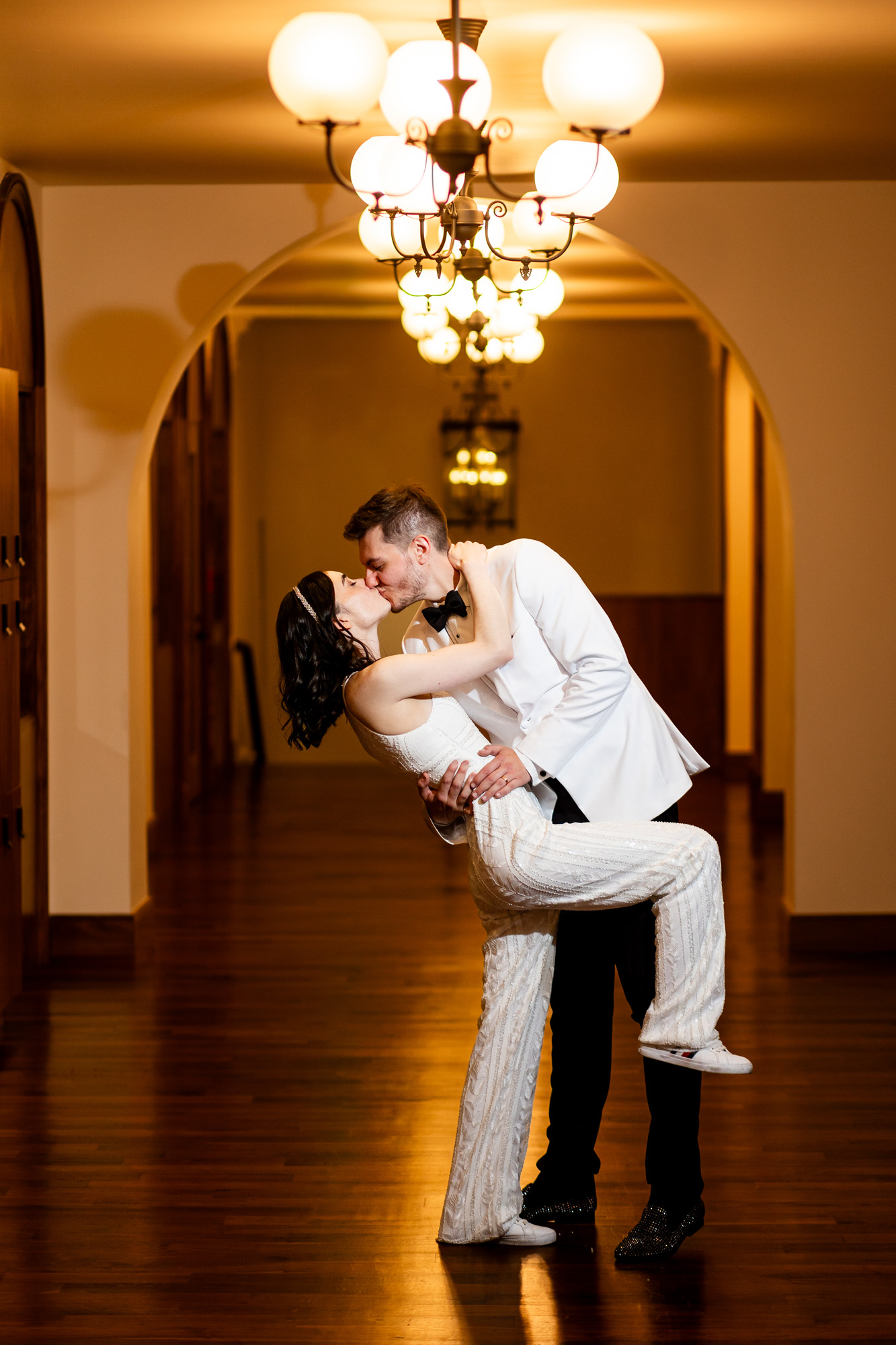 Bride and groom share a kiss while being dipped in a warmly lit hallway beneath a chandelier Colorado Wedding Photographer Colorado Wedding Photographer