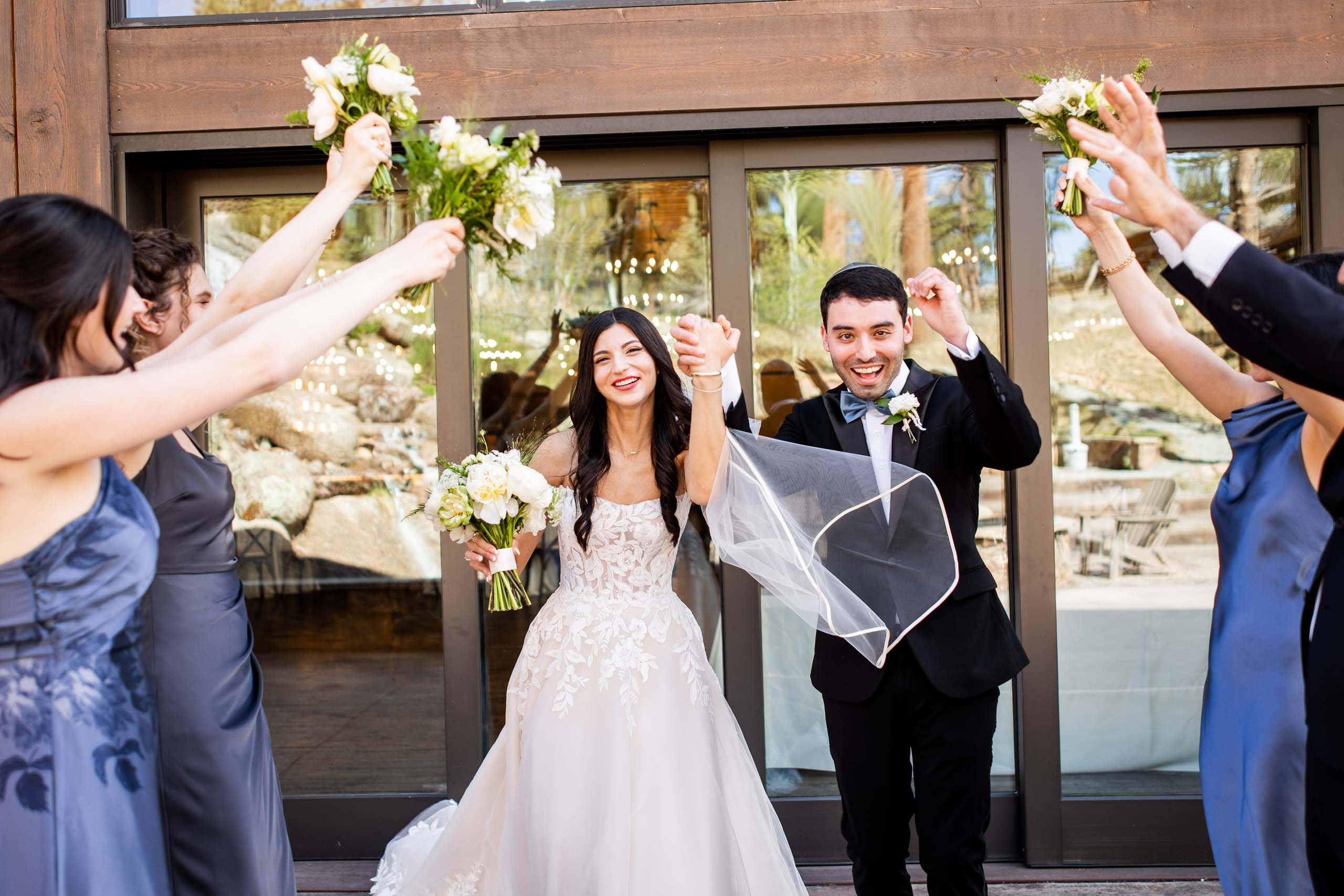 Bride and groom celebrate outside raising bouquets with smiling attendants surrounding them Colorado Wedding Photographer Colorado Wedding Photographer