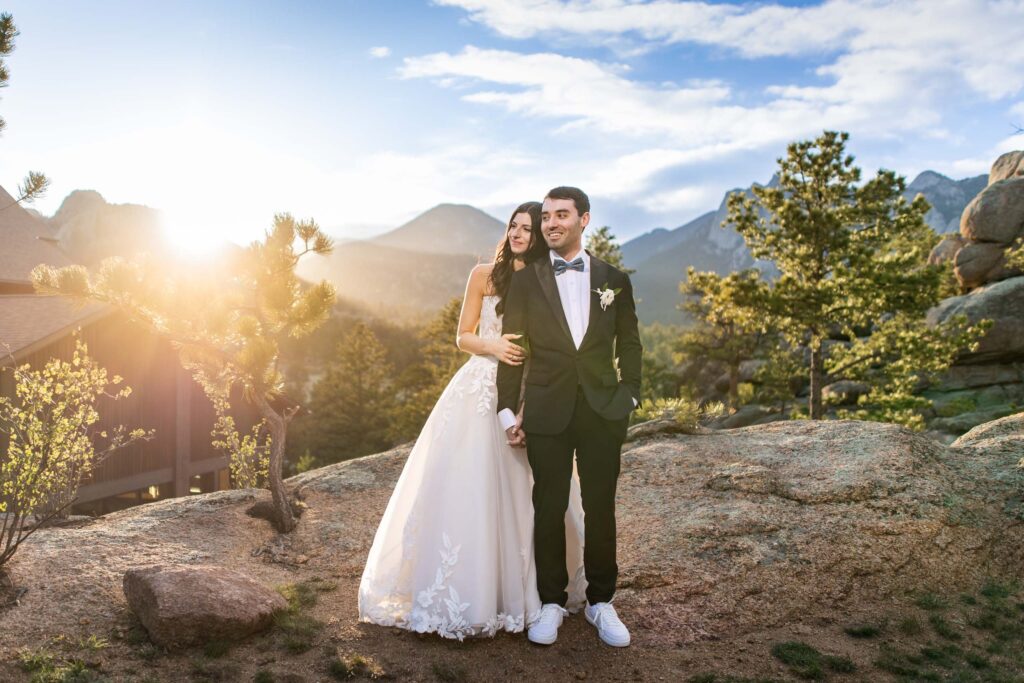 Couple in wedding attire standing on rocky ground with mountains and trees at sunset in the background Colorado Wedding Photographer Colorado Wedding Photographer
