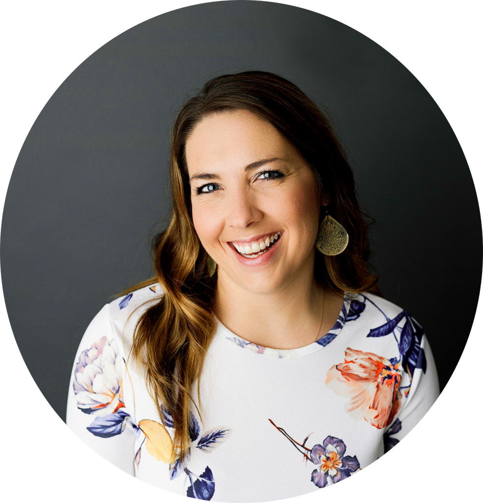 Smiling woman with long brown hair wearing a white floral blouse against a dark gray backdrop round crop portrait Colorado Wedding Photographer Colorado Wedding Photographer