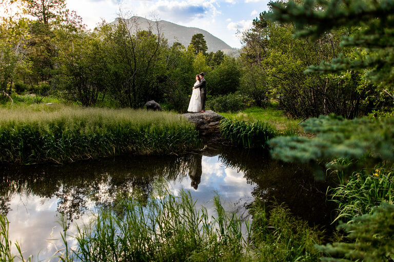 Wedding couple standing on rock with mountains in background at Riversong Inn Retreat Colorado Wedding Photographer Colorado Wedding Photographer